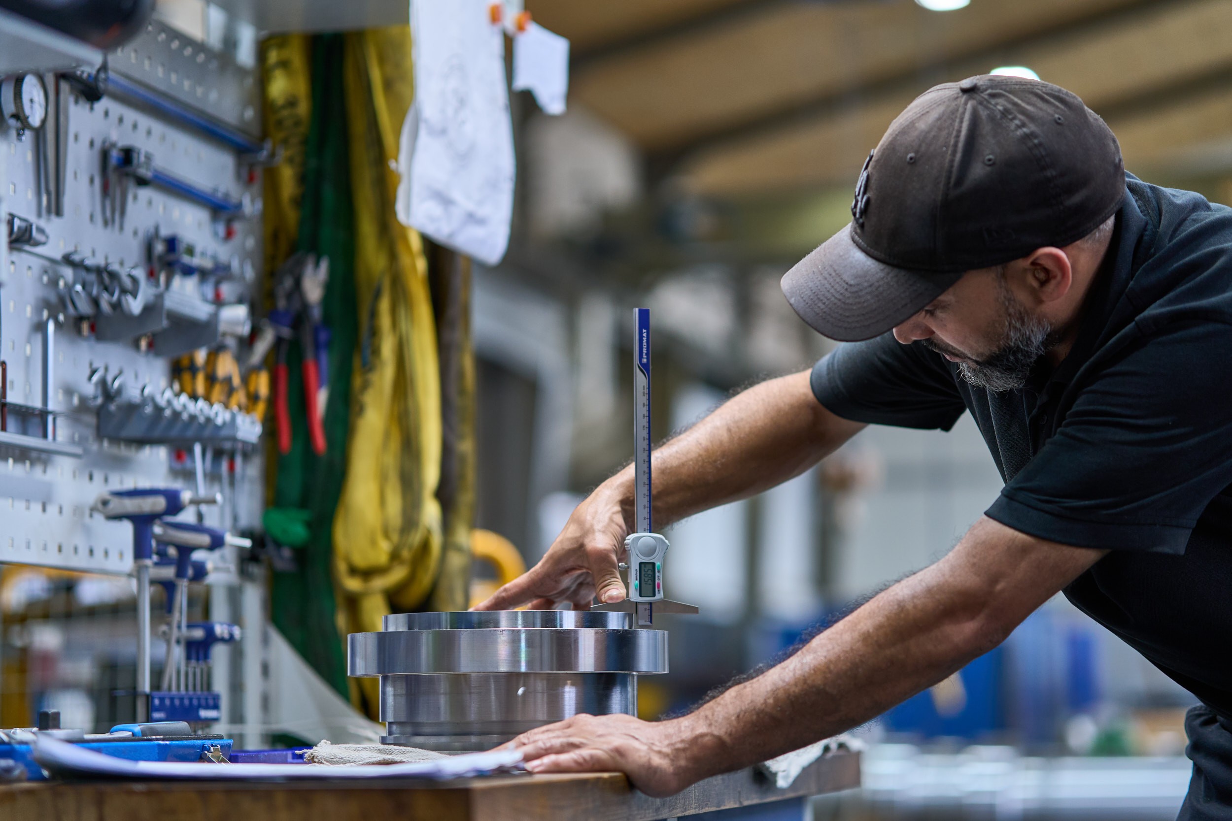 Auf einer Werkbank f&uuml;hrt ein Mitarbeiter von ACONA Messungen an einem Bauteil eines Hydraulikzylinders durch